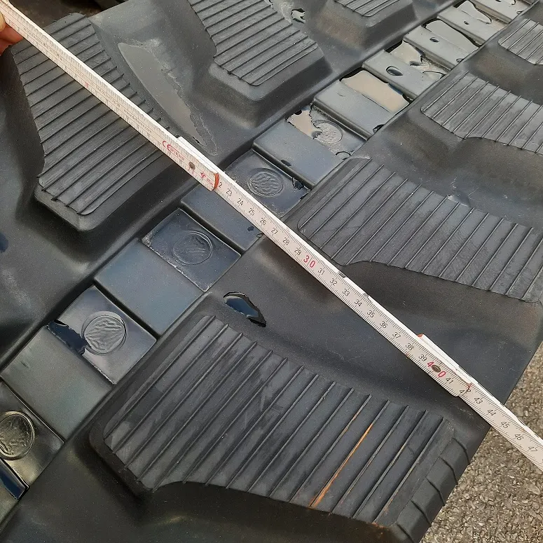 De rupsbreedte van de rubberen rups wordt opgemeten met een duimstok meter.